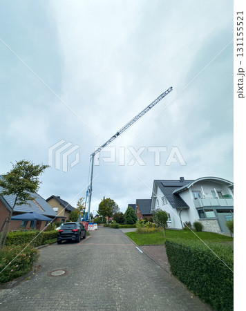Construction crane towers over residential area during cloudy day with nearby homes and parked vehicle in view 131155521