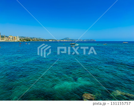 Vibrant blue waters and boats dotting the coastline of a sunny beach in a scenic location during a clear summer day Vibrant blue waters and boats dotting the coastline of a sunny beach in a scenic location during a clear summer day 131155757