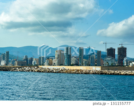 Construction and development along the shoreline of a coastal city under a blue sky with mountains in the distance Construction and development along the shoreline of a coastal city under a blue sky with mountains in the distance 131155777