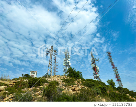 Communication towers and power lines stand tall against a blue sky with scattered clouds, captured on a sunny day in a rural area 131155782
