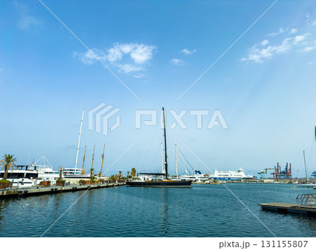 Sailboats and yachts gently sway in the harbor under a sunny sky with fluffy clouds above Sailboats and yachts gently sway in the harbor under a sunny sky with fluffy clouds above 131155807