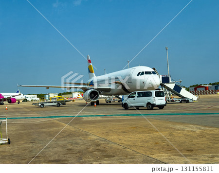 Airplane parked on tarmac at a busy airport with service vehicles and clear blue sky in the background during daytime Airplane parked on tarmac at a busy airport with service vehicles and clear blue sky in the background during daytime 131155811