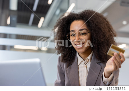 Close-up photo of a young African-American woman working in an office using a laptop, using a credit card in her hand. 131155851