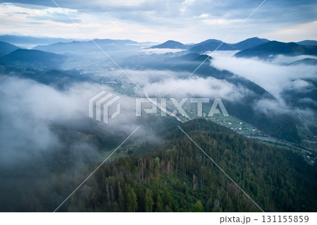 Breathtaking aerial view of valley enveloped in morning mist, with river winding through lush green hills and village nestled among trees. 131155859