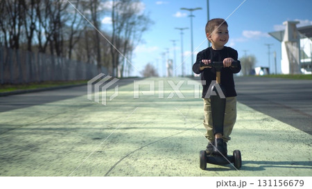 A child joyfully riding their scooter on a sunny day in a beautiful park filled with nature A child joyfully riding their scooter on a sunny day in a beautiful park filled with nature 131156679