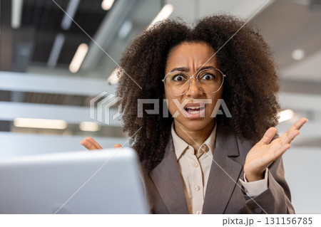 Close-up portrait of a young African-American angry woman sitting in the office at her desk and casually waving her arms at the camera. Close-up portrait of a young African-American angry woman sitting in the office at her desk and casually waving her arms at the camera. 131156785