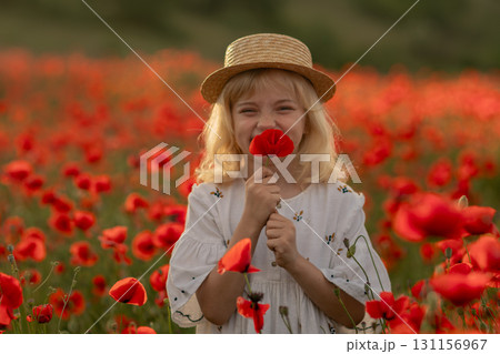 A young girl is standing in a field of red poppies, holding a flower in her hand A young girl is standing in a field of red poppies, holding a flower in her hand 131156967