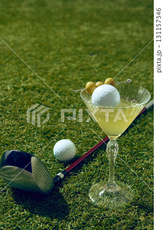 Close up of martini cocktail with golf ball and olives on grass field 131157346