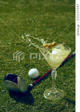 Golf ball splashes inside martini cocktail on grass with club and another ball Golf ball splashes inside martini cocktail on grass with club and another ball 131157347