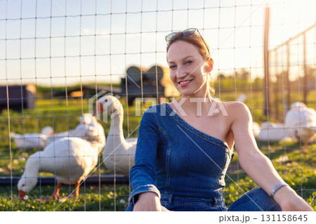 Portrait young adult happy smiling woman wear jeans denim jumpsuit enjoy having fun countryside farm animal geese flock warm sunset light. Female person rural country village farmyard bird poultry Portrait young adult happy smiling woman wear jeans denim jumpsuit enjoy having fun countryside farm animal geese flock warm sunset light. Female person rural country village farmyard bird poultry 131158645