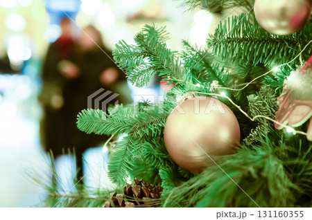 christmas tree decorated with garlands and balls on a blurred background of a couple walking along a festive street 131160355