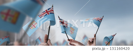 Fiji flags in their hands on a blurred urban background 131160420