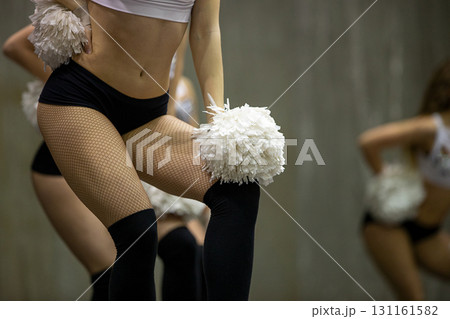 Cheerleader girl in black fishnet tights and shorty shorts with white pompoms in her hands 131161582