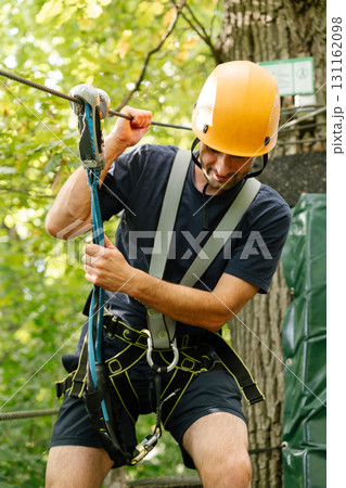 Man adjusting climbing rope at forest zipline Man adjusting climbing rope at forest zipline 131162098