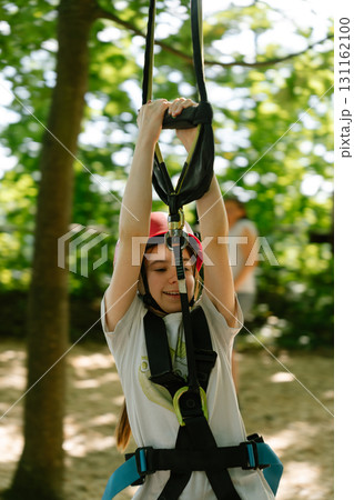 Girl on zipline rope course with helmet and safety harness, outdoor climbing activity Girl on zipline rope course with helmet and safety harness, outdoor climbing activity 131162100