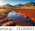 The shallow puddle surrounded with red stone floor in a desert with the mountains in the background. 131162633