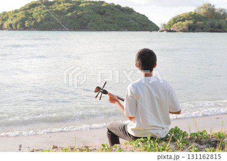 海岸で三線を奏でる少年 131162815