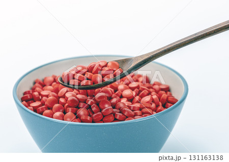 Blue bowl of red pills with wooden spoon, symbolizing daily medicine as food and healthcare lifestyle concept. 131163138
