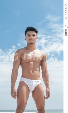 Fit Asian man in swim shorts standing on a tropical beach with a clear blue sky Fit Asian man in swim shorts standing on a tropical beach with a clear blue sky 131163482
