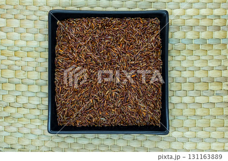 Red Rice Grains in Black Plate on Natural Bamboo Mat Background Surface with Free Space Red Rice Grains in Black Plate on Natural Bamboo Mat Background Surface with Free Space 131163889