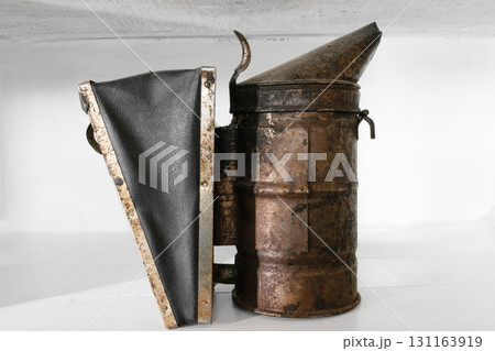 Rusty, dusty and very old bee smoker placed on white shelf 131163919