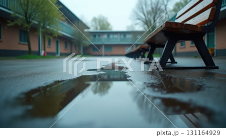 Empty Schoolyard After Rain with Flag Reflection in Puddle and Overturned Bench Empty Schoolyard After Rain with Flag Reflection in Puddle and Overturned Bench 131164929