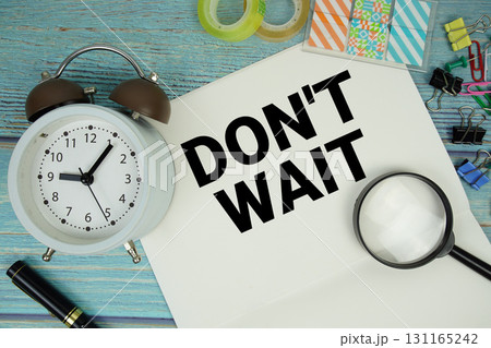 Don't Wait text written on notepad with alarm clock and magnifying glass flat lay on wooden background 131165242