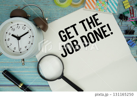 Get The Job Done! text on a paper surrounded by office supplies, a magnifying glass, and a clock on a blue wooden surface Get The Job Done! text on a paper surrounded by office supplies, a magnifying glass, and a clock on a blue wooden surface 131165250