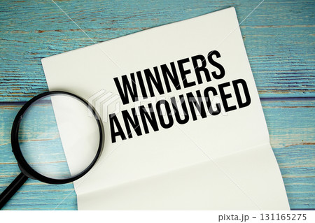 Winners Announced text written on notepad with magnifying glass flat lay on wooden background 131165275