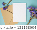 Empty white blank greeting or invitation card with envelope and violet flower decoration on blue background. 131168004