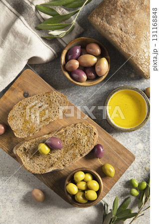 Mediterranean snack with mixed olives, olive oil, and rustic bread on wooden board. 131168848