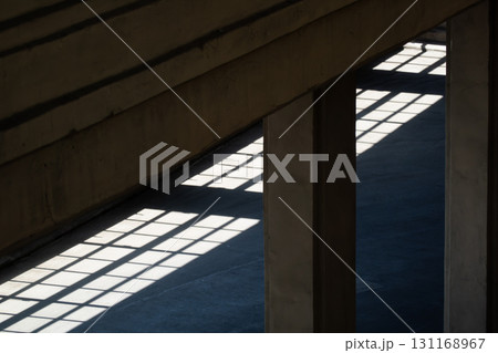 Industrial light and shadow play along concrete pillars in sunlit grid pattern 131168967