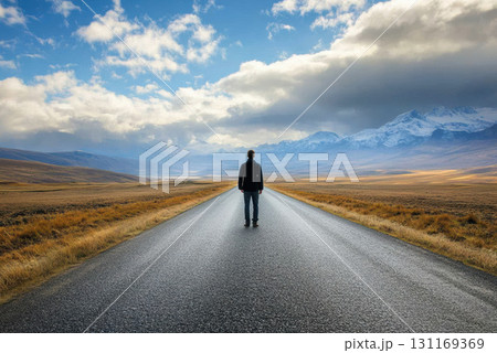person standing at start of long road, surrounded by mountains and open fields, evokes sense of adventure and exploration 131169369