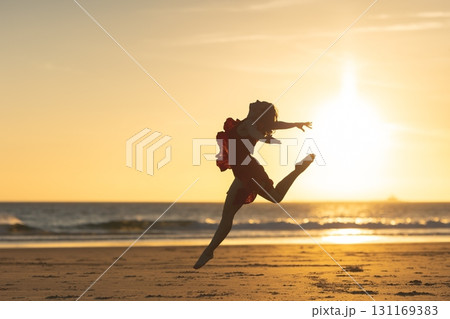 Ballerina jumping on the beach at sunset, embracing freedom and dance 131169383