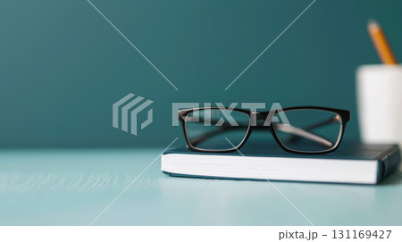 Glasses resting on book with pencil and cup in background, creating calm study atmosphere 131169427