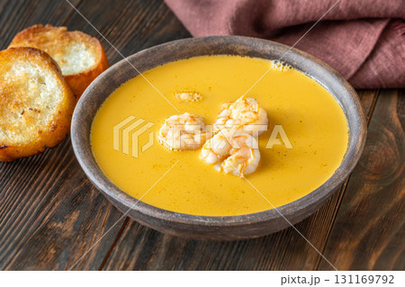Rustic shrimp bisque with toasted baguette slices beside clay bowl 131169792