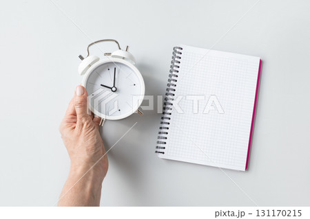 Alarm clock in woman hand and empty sheet blank on gray background. Daily routine. View from above. Copy space. 131170215