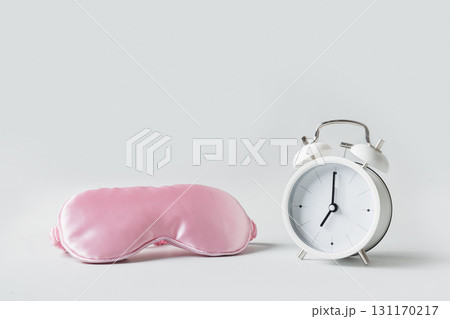 Soft contoured eye mask for comfortable sleep. Pink mask and white alarm clock on gray background. Concept of sleep, insomnia, health care, daily routine and circadian rhythms. Can't fall asleep. 131170217