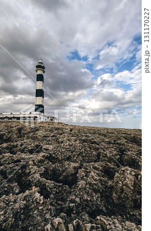 Tall black and white lighthouse standing on rocky shore 131170227