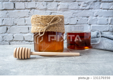 Honey jar with honeycomb, cap of tee and wood spoon stay on the table near napkin. 131170350