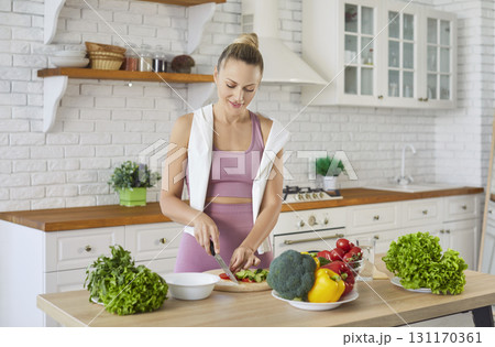 Modern indoor kitchen, happy fit woman wearing fitness attire standing and cutting vegetables Modern indoor kitchen, happy fit woman wearing fitness attire standing and cutting vegetables 131170361