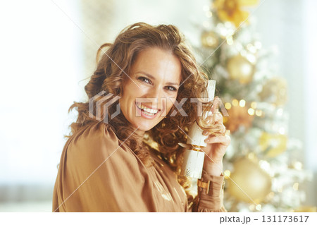Woman Holds Christmas Cracker by Festive Tree 131173617