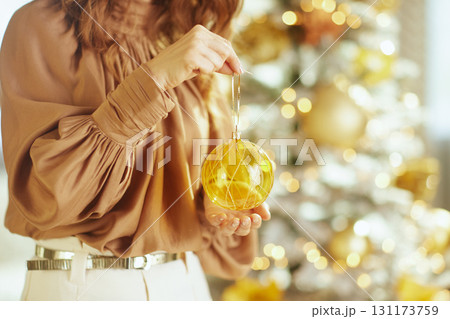 Woman\'s Hands Adorn Christmas Tree with Gold Bauble 131173759