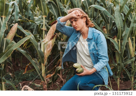 Sad farmer holding corn cobs and suffering from heat stroke in cultivated cornfield Sad farmer holding corn cobs and suffering from heat stroke in cultivated cornfield 131173912