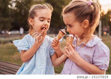Two little girls enjoying ice cream cones in a park Two little girls enjoying ice cream cones in a park 131173919