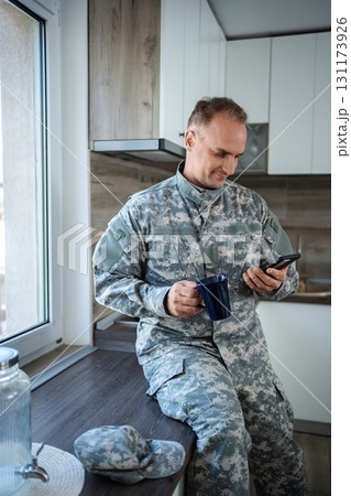 Soldier enjoying a coffee break and checking his phone in the kitchen Soldier enjoying a coffee break and checking his phone in the kitchen 131173926