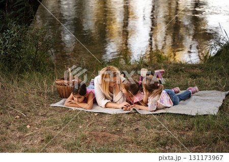 Mother Lying with her Three Daughters by the River Having a Picnic 131173967