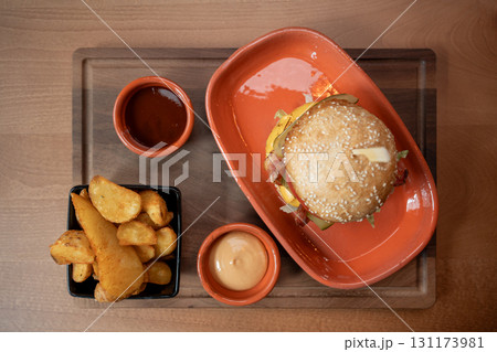 Delicious burger with golden fries and dipping sauces on a rustic wooden tray Delicious burger with golden fries and dipping sauces on a rustic wooden tray 131173981