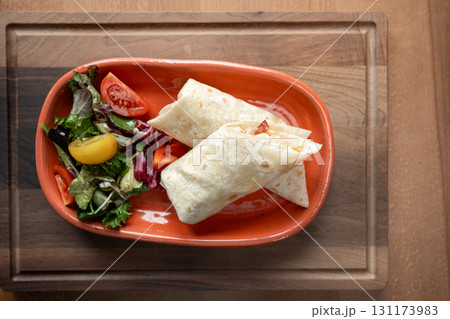 Delicious wrap served on a vibrant plate with fresh garden salad 131173983