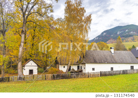 Autumn scenery with a traditional white house and trees with yellow leaves against a mountainous backdrop. The Liptov region in Slovakia, Europe. Autumn scenery with a traditional white house and trees with yellow leaves against a mountainous backdrop. The Liptov region in Slovakia, Europe. 131174540